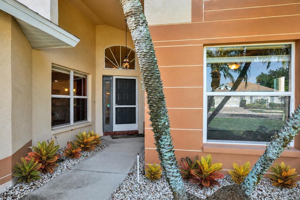 A concrete walkway leads to the front entrance of a house with orange stucco walls — 2023 PRESTANCIA LANE, SUN CITY CENTER, FL