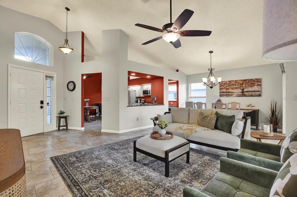 A living room features tile floors, a vaulted ceiling with a fan, and an adjacent kitchen — 2023 PRESTANCIA LANE, SUN CITY CENTER, FL