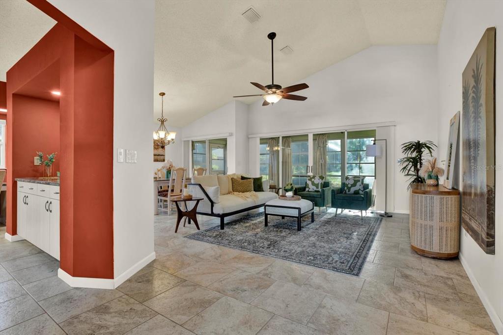 A living room with tile floors, a vaulted ceiling, and a view of the dining area — 2023 PRESTANCIA LANE, SUN CITY CENTER, FL