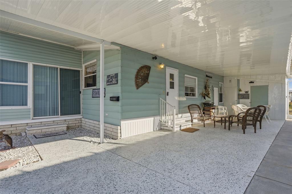 A light blue mobile home features a large covered carport, concrete patio, and outdoor seating — 82403 NEW CIRCLE DRIVE N, PINELLAS PARK, FL