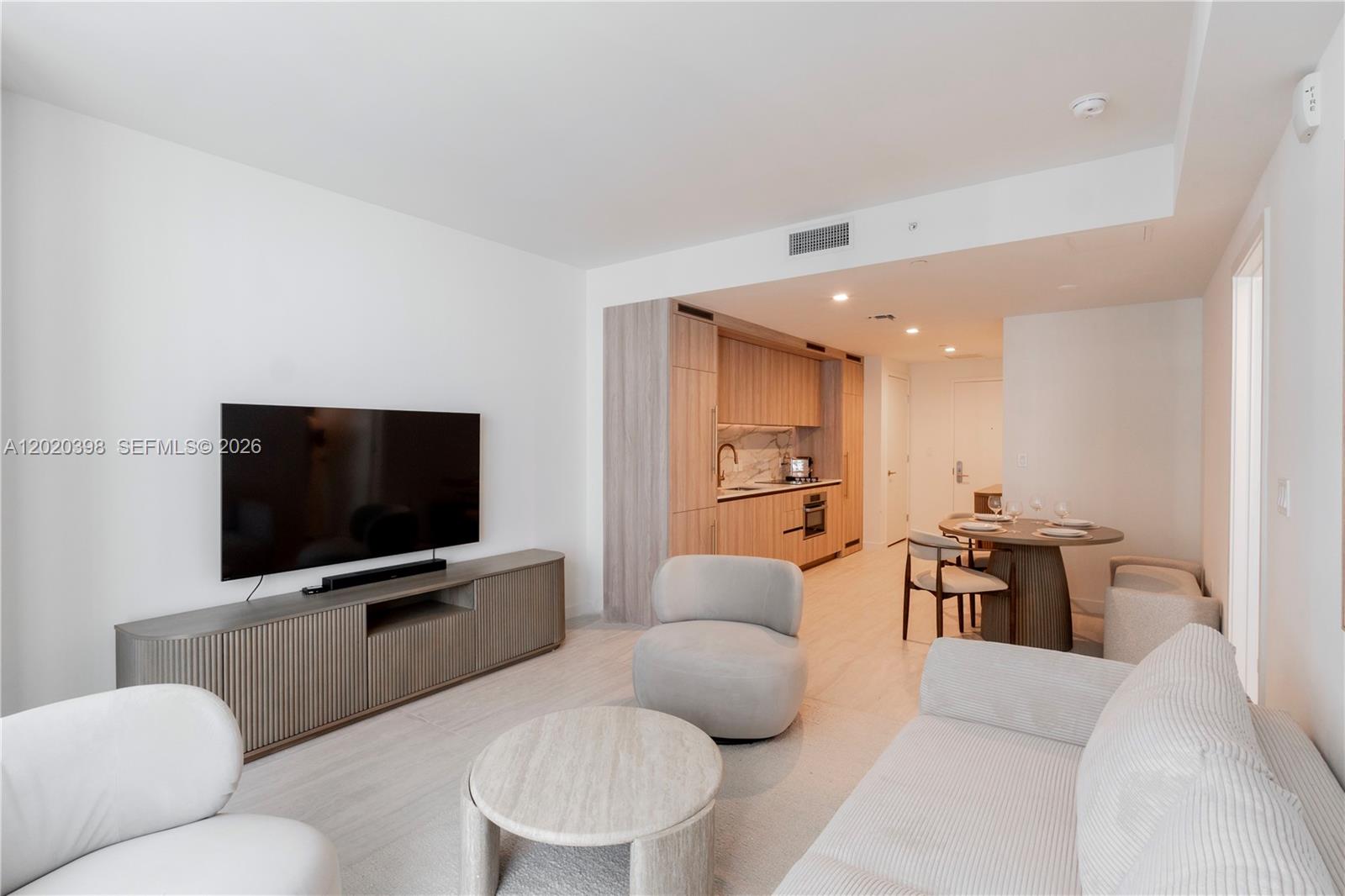 A modern living room features a television console, light-colored furniture, and an open-concept kitchen — 77 SE 5th St # 1910, Miami FL 33131, MIAMI, FL