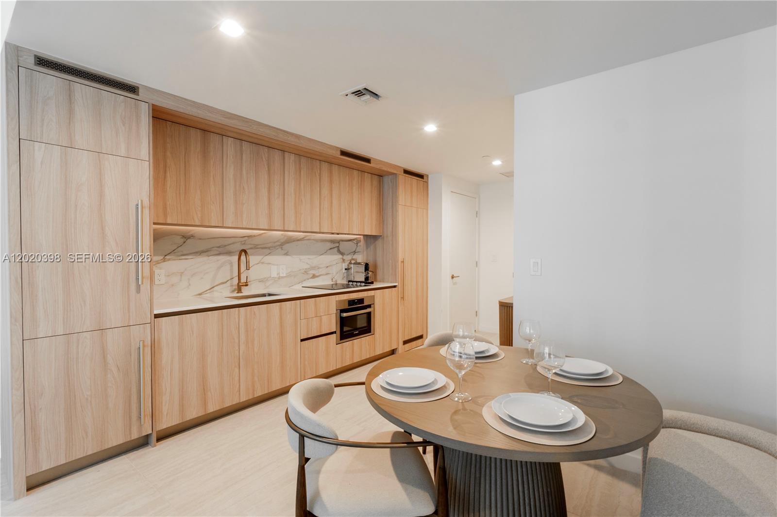 A modern kitchen features light wood cabinetry, marble backsplash, and an adjacent round dining table — 77 SE 5th St # 1910, Miami FL 33131, MIAMI, FL