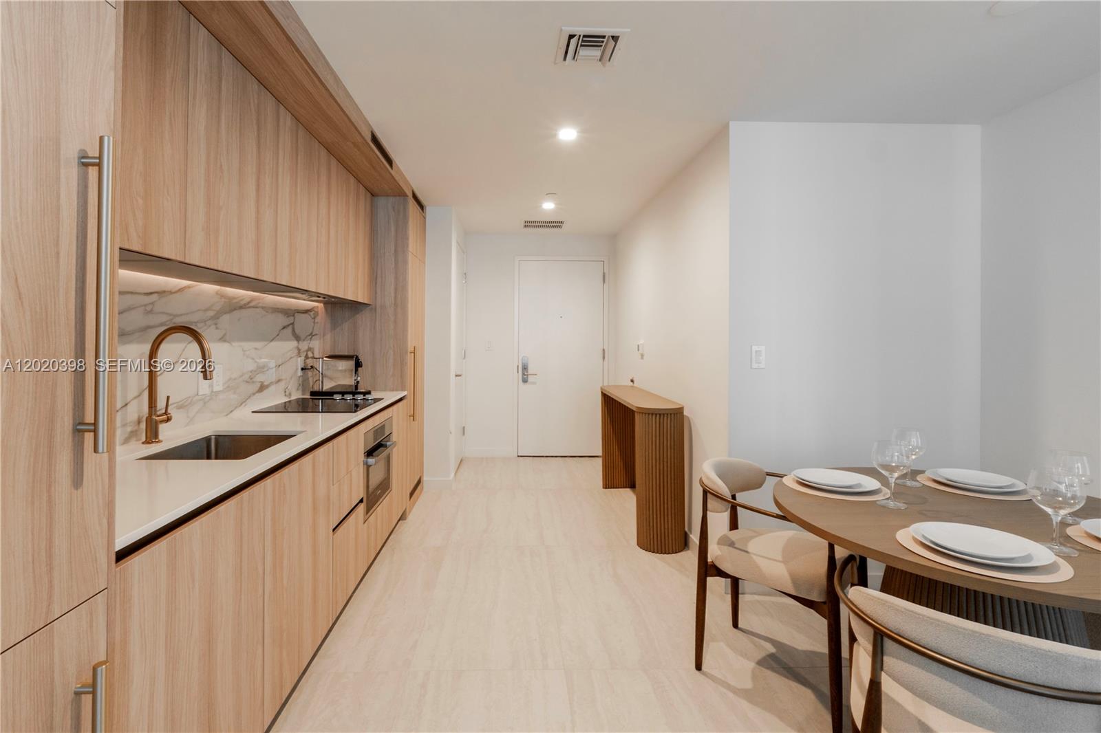 A modern kitchen features light wood cabinetry, marble backsplash, and an adjacent dining area — 77 SE 5th St # 1910, Miami FL 33131, MIAMI, FL