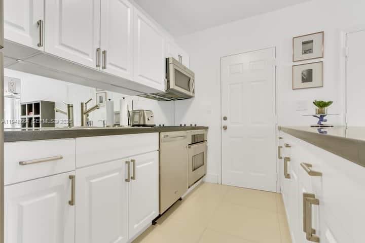 A galley kitchen features white cabinets, stainless steel appliances, and light-colored tile flooring — 290 Sunrise # 206, Key Biscayne FL 33149, KEY BISCAYNE, FL