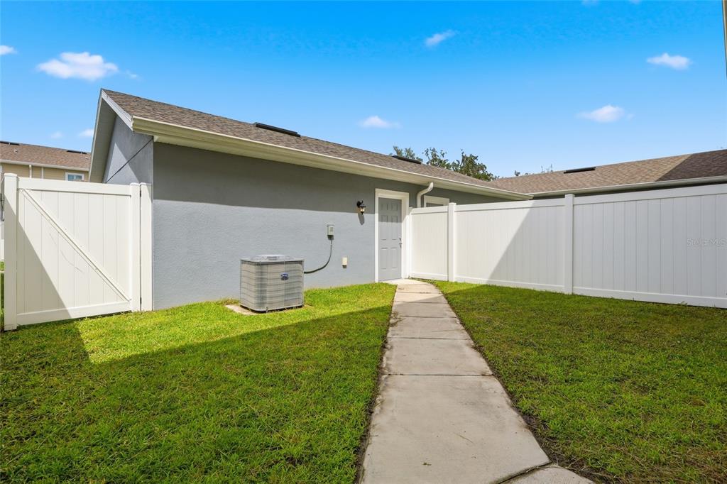 A gray house exterior features a white door, an air conditioning unit, and white fencing — 5106 SEA MIST LANE, WESLEY CHAPEL, FL