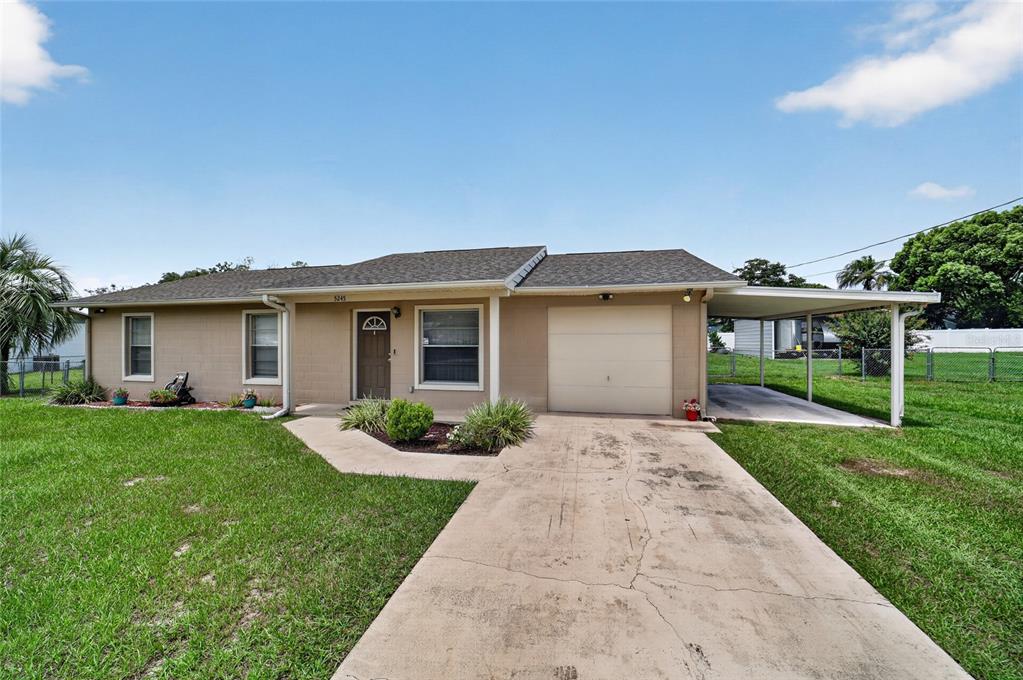 A single-story tan house with a concrete driveway, attached garage, and a side carport — 5245 SE 107TH PLACE, BELLEVIEW, FL