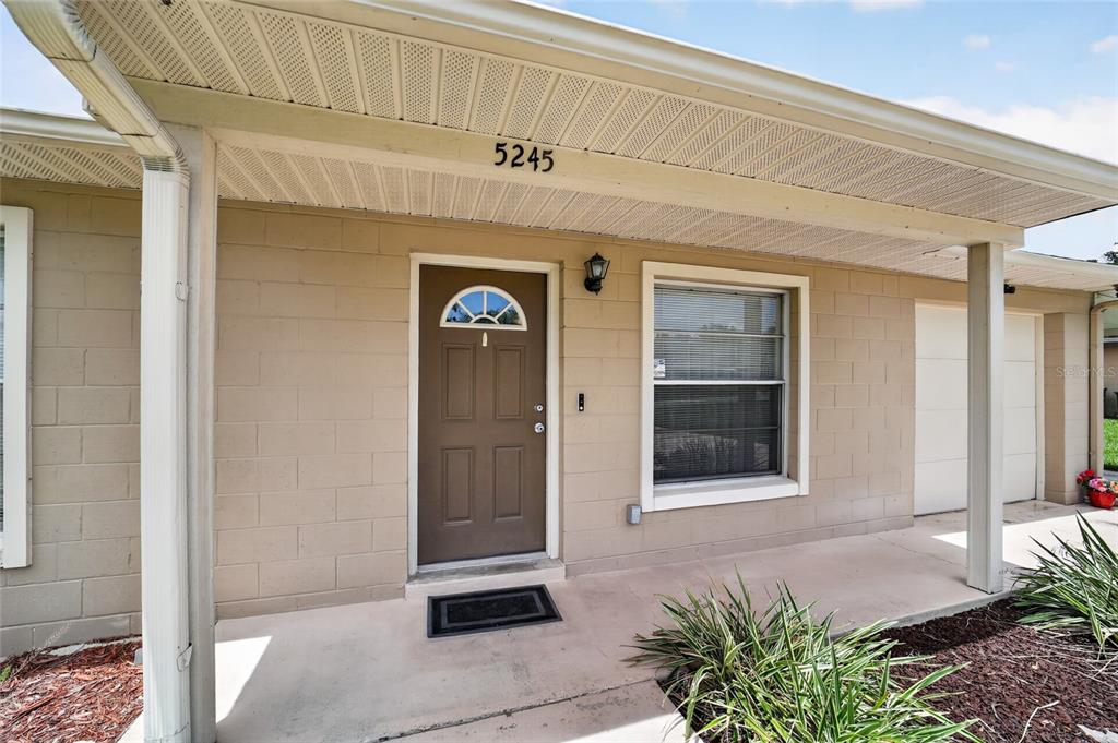 The exterior of a beige concrete block house features a brown front door and porch — 5245 SE 107TH PLACE, BELLEVIEW, FL