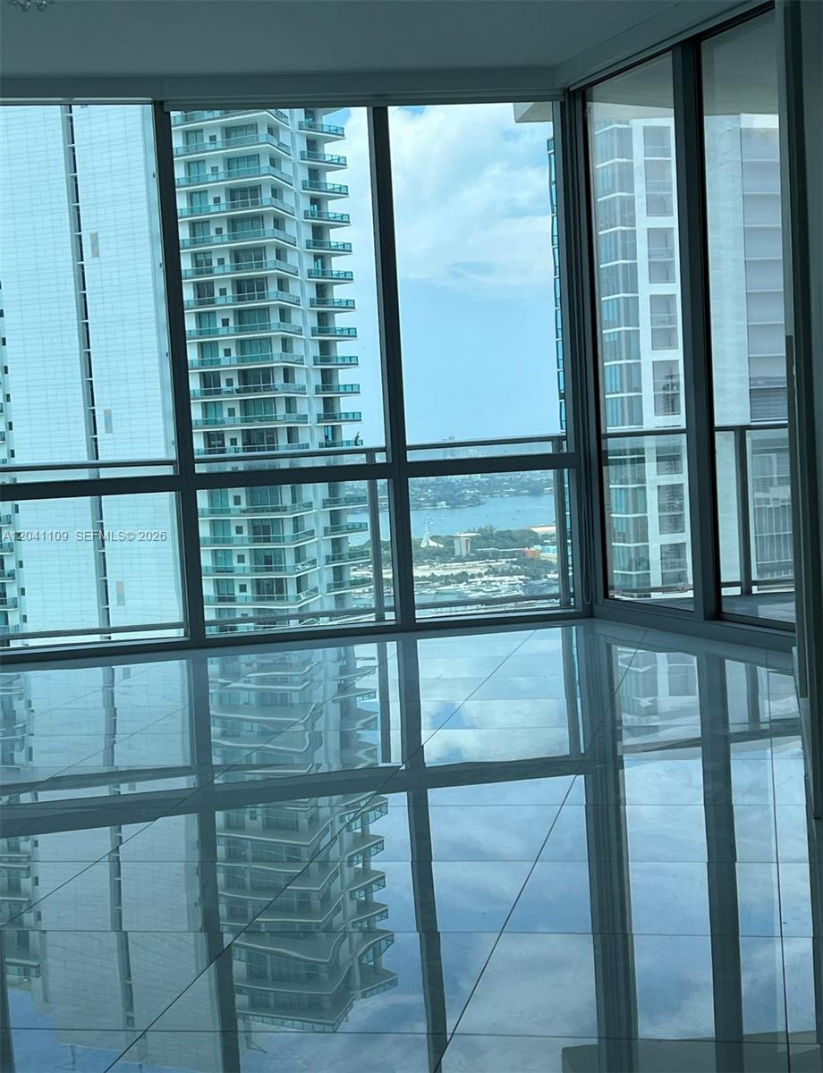 An empty room with white tile floors features floor-to-ceiling windows overlooking city buildings and water — 851 NE 1st Ave # 3803, Miami FL 33132, MIAMI, FL