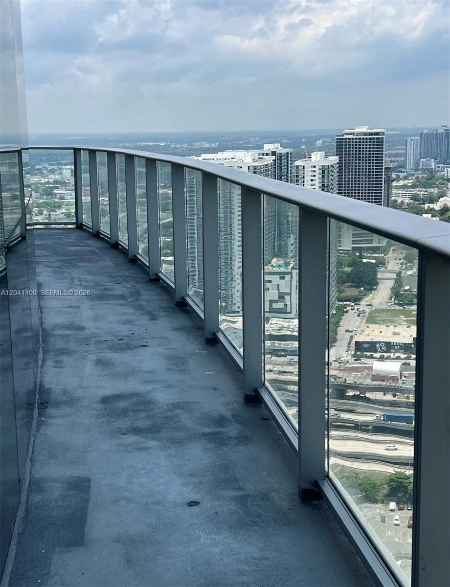 A curved balcony with glass railings overlooks a city skyline and highway — 851 NE 1st Ave # 3803, Miami FL 33132, MIAMI, FL
