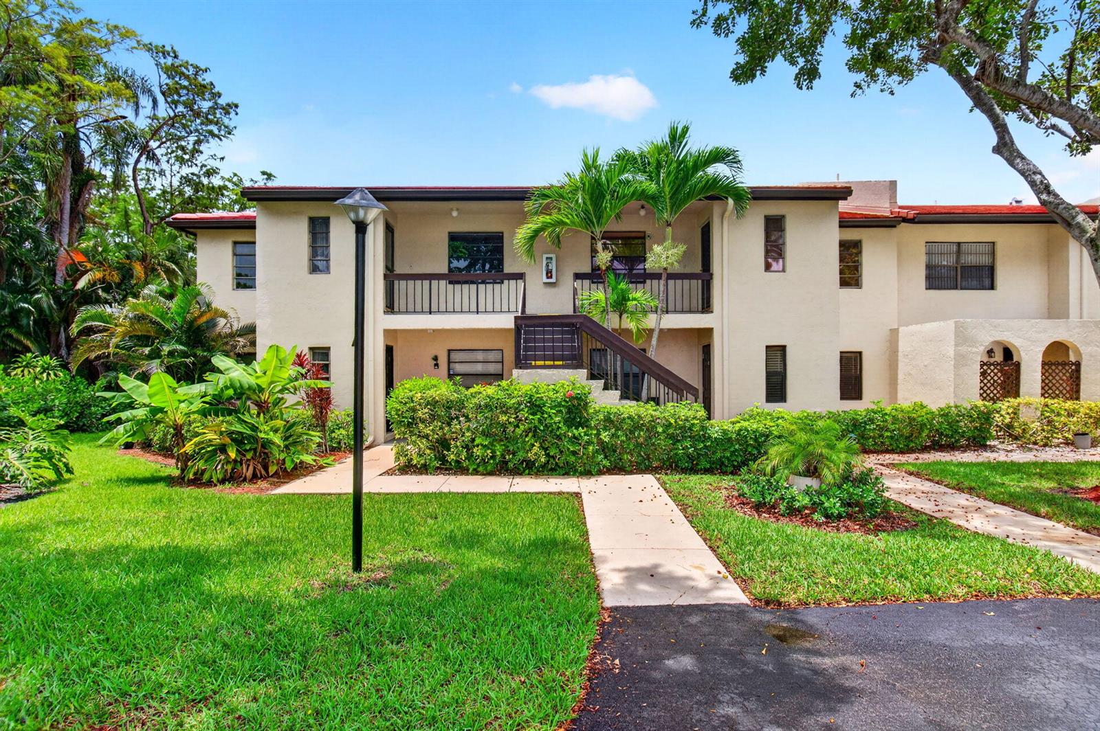 A two-story apartment building with beige stucco walls, a central staircase, and surrounding landscaping — 8460 Casa Del Lago, Boca Raton FL 33433, BOCA RATON, FL