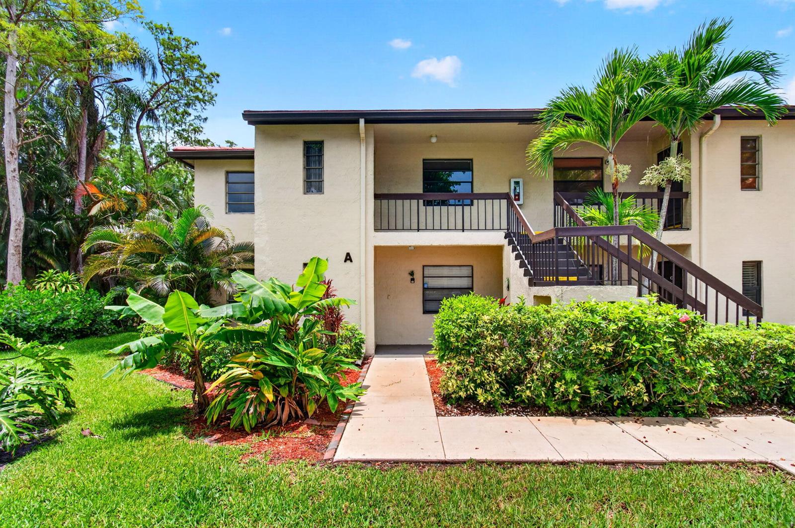 A two-story apartment building exterior with a concrete walkway, tropical landscaping, and an outdoor staircase — 8460 Casa Del Lago, Boca Raton FL 33433, BOCA RATON, FL