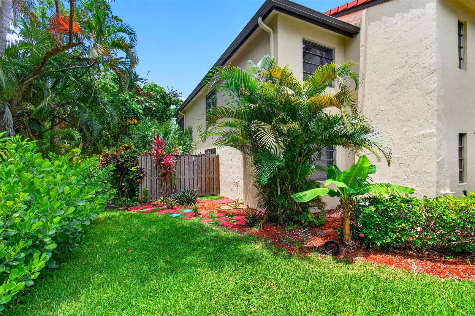 A side view of a beige stucco building with palm trees and a wooden fence — 8460 Casa Del Lago, Boca Raton FL 33433, BOCA RATON, FL