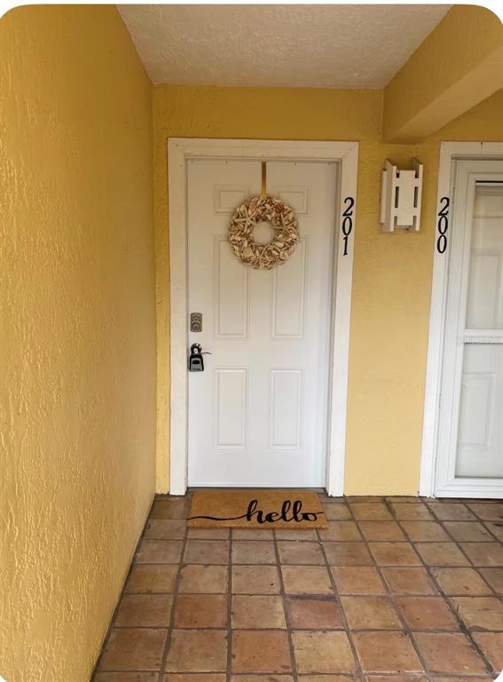 An exterior view of a yellow building entrance featuring a white door with a wreath — 1125 PINELLAS BAYWAY S UNIT 201 furnished, ST PETERSBURG, FL