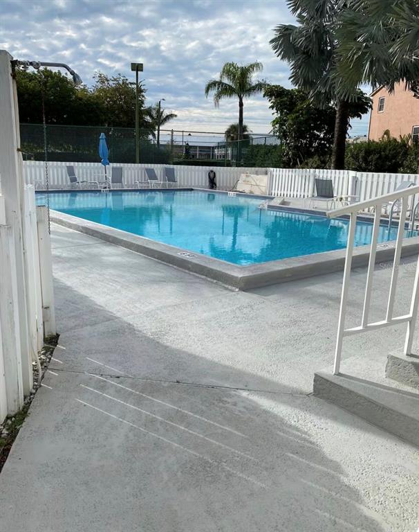 A rectangular outdoor swimming pool is surrounded by a white fence and concrete deck — 1125 PINELLAS BAYWAY S UNIT 201 furnished, ST PETERSBURG, FL