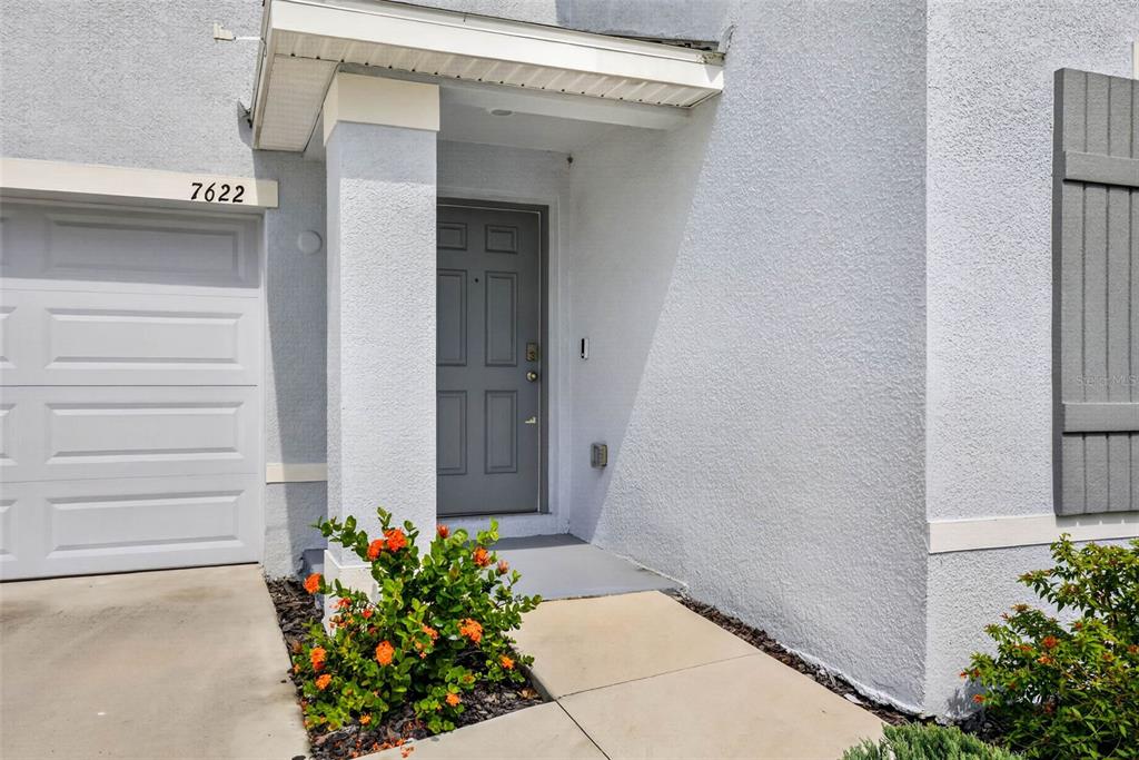 A gray front door is recessed under a small porch next to a garage — 7622 ROSEWOOD GARDEN LOOP, TAMPA, FL