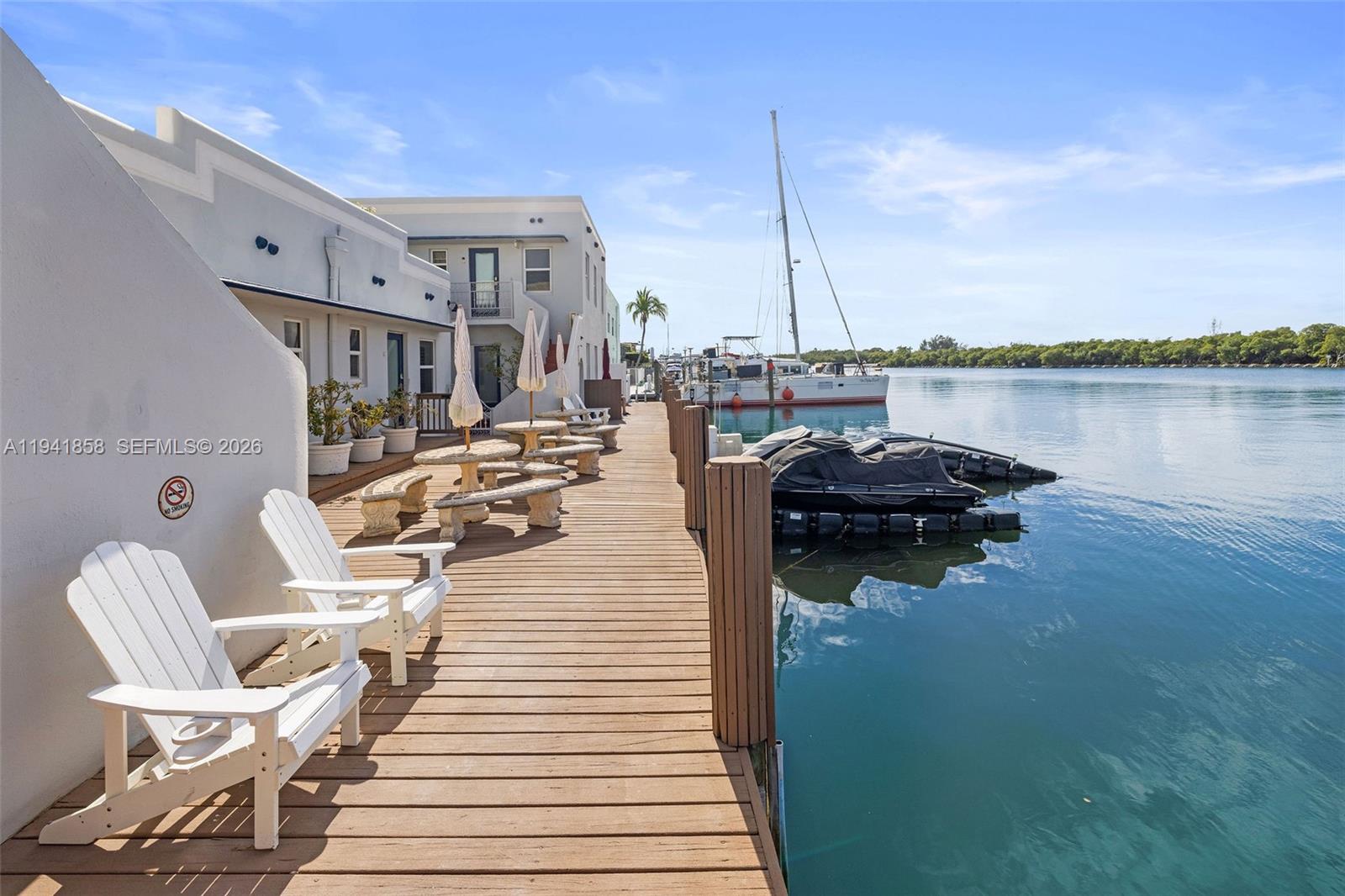 A wooden dock features white Adirondack chairs, outdoor seating, and a view of the water — 1908 N Ocean Dr, Hollywood FL 33019, HOLLYWOOD, FL