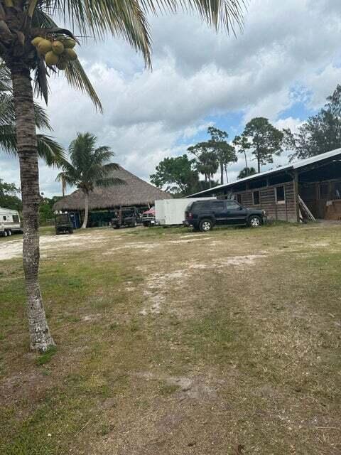 A palm tree stands in the foreground of a grassy lot with a large tiki hut — 3525 D Rd Road, FL 33470, FL
