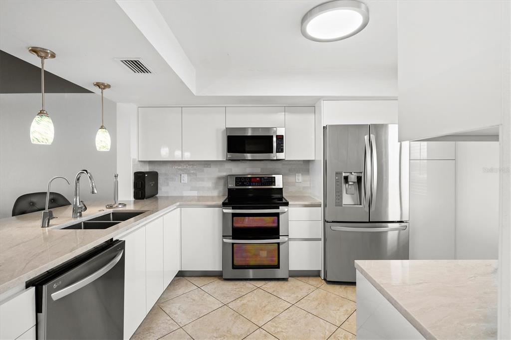 A modern kitchen with white cabinets, stainless steel appliances, and beige tile flooring — 9604 CORTEZ ROAD W UNIT 134, BRADENTON, FL