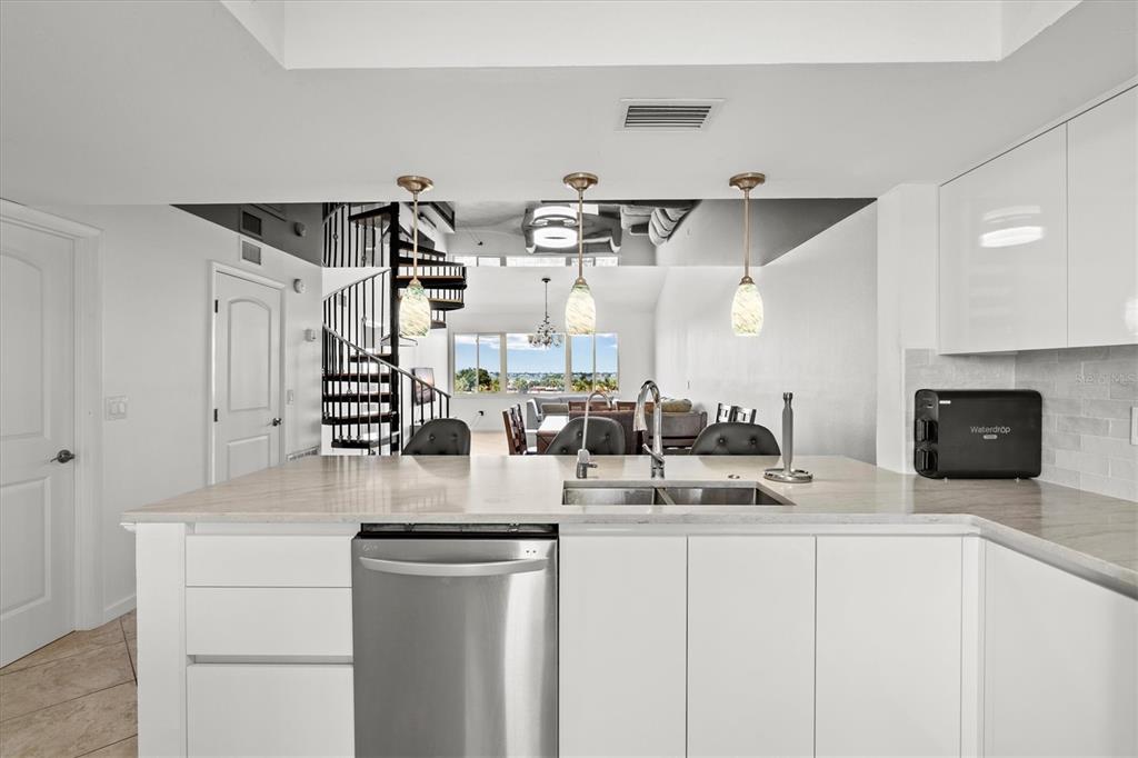 A modern kitchen with white cabinets and a stainless steel dishwasher overlooks a living area — 9604 CORTEZ ROAD W UNIT 134, BRADENTON, FL