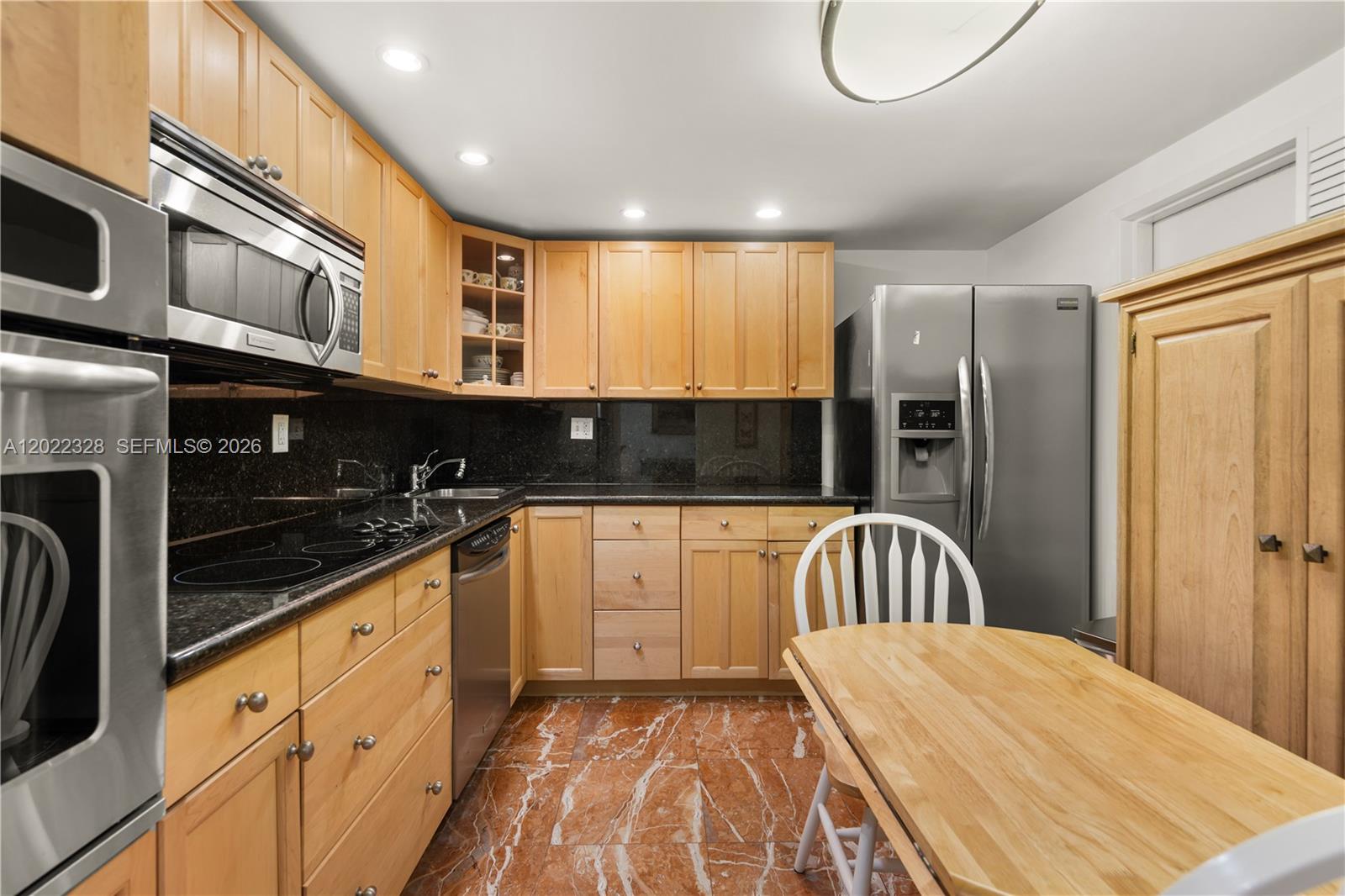 A kitchen features light wood cabinets, black countertops, stainless steel appliances, and marble-patterned tile flooring — 210 Sea View Dr # 611, Key Biscayne FL 33149, KEY BISCAYNE, FL