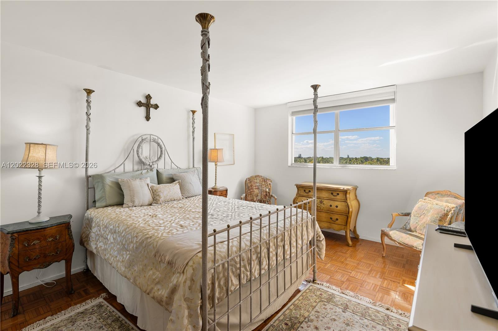 A bedroom features a metal canopy bed, parquet wood flooring, and a window with views — 210 Sea View Dr # 611, Key Biscayne FL 33149, KEY BISCAYNE, FL