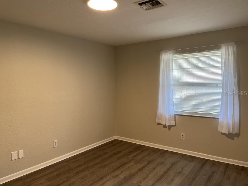 An empty bedroom features light-colored walls, wood-look flooring, a window with white curtains, and a ceiling light — 624 GOLDEN RAINTREE PLACE UNIT 624, BRANDON, FL