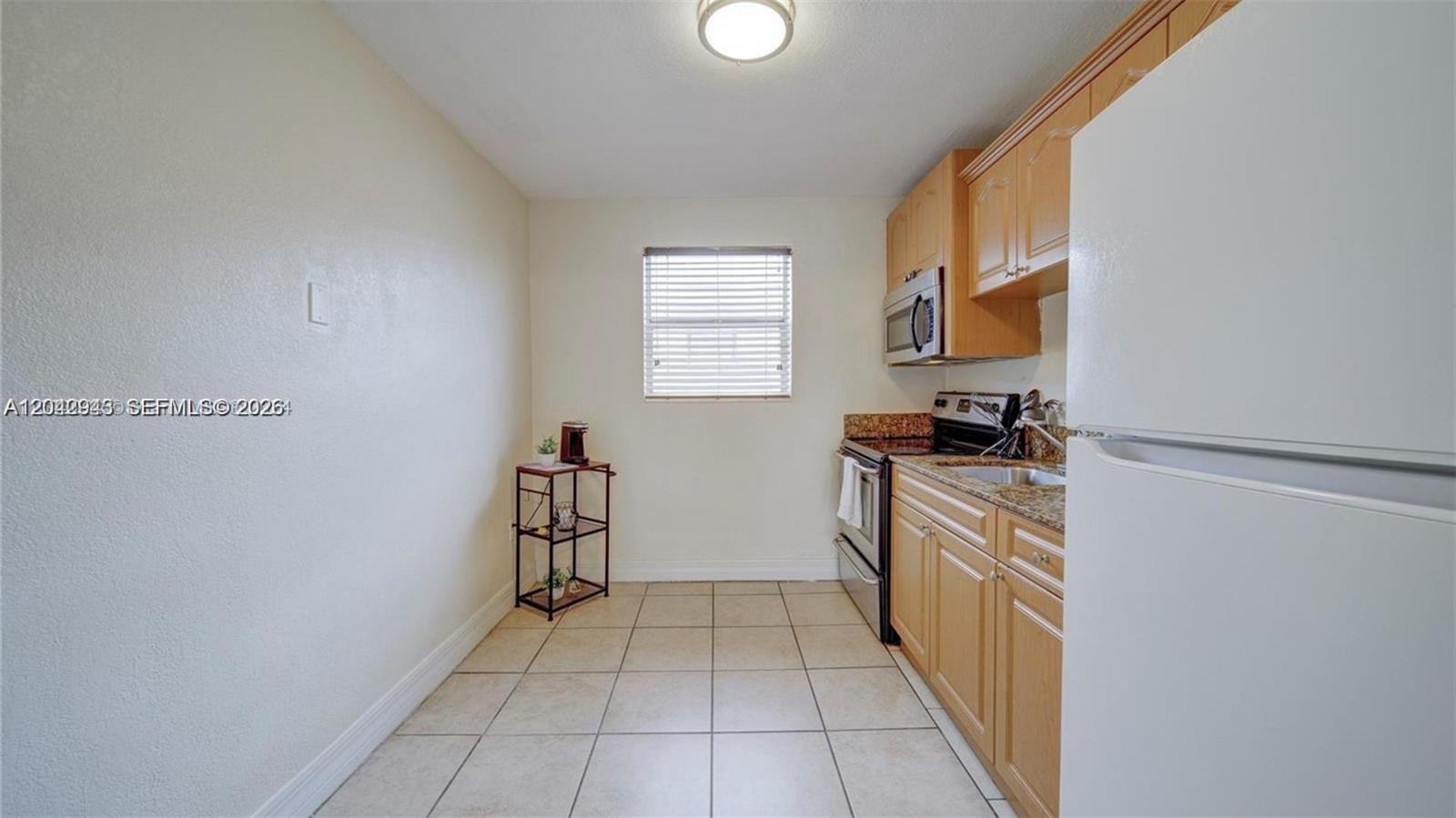 A kitchen features light wood cabinets, granite countertops, tile flooring, and a white refrigerator — 427 SW 6th St # 4, Miami FL 33130, MIAMI, FL
