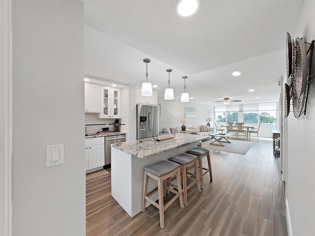 An open-concept kitchen with a granite island and bar stools overlooks a living and dining area — 2620 COVE CAY DRIVE UNIT 403, CLEARWATER, FL