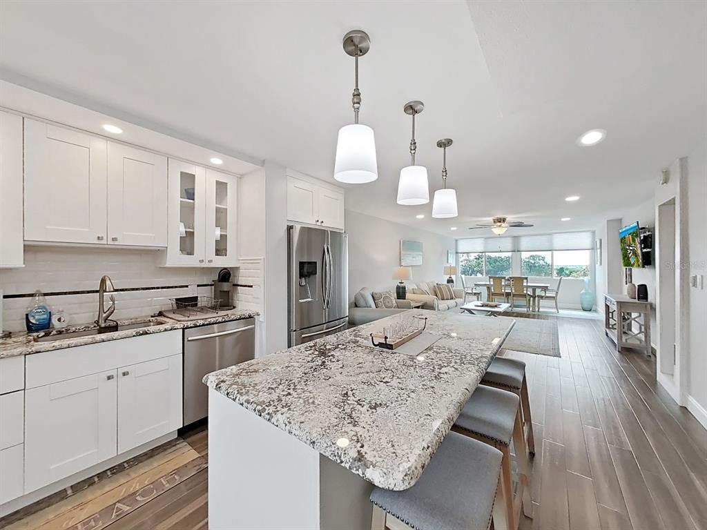 A modern kitchen with white cabinets, granite countertops, and an island opens to a living area — 2620 COVE CAY DRIVE UNIT 403, CLEARWATER, FL
