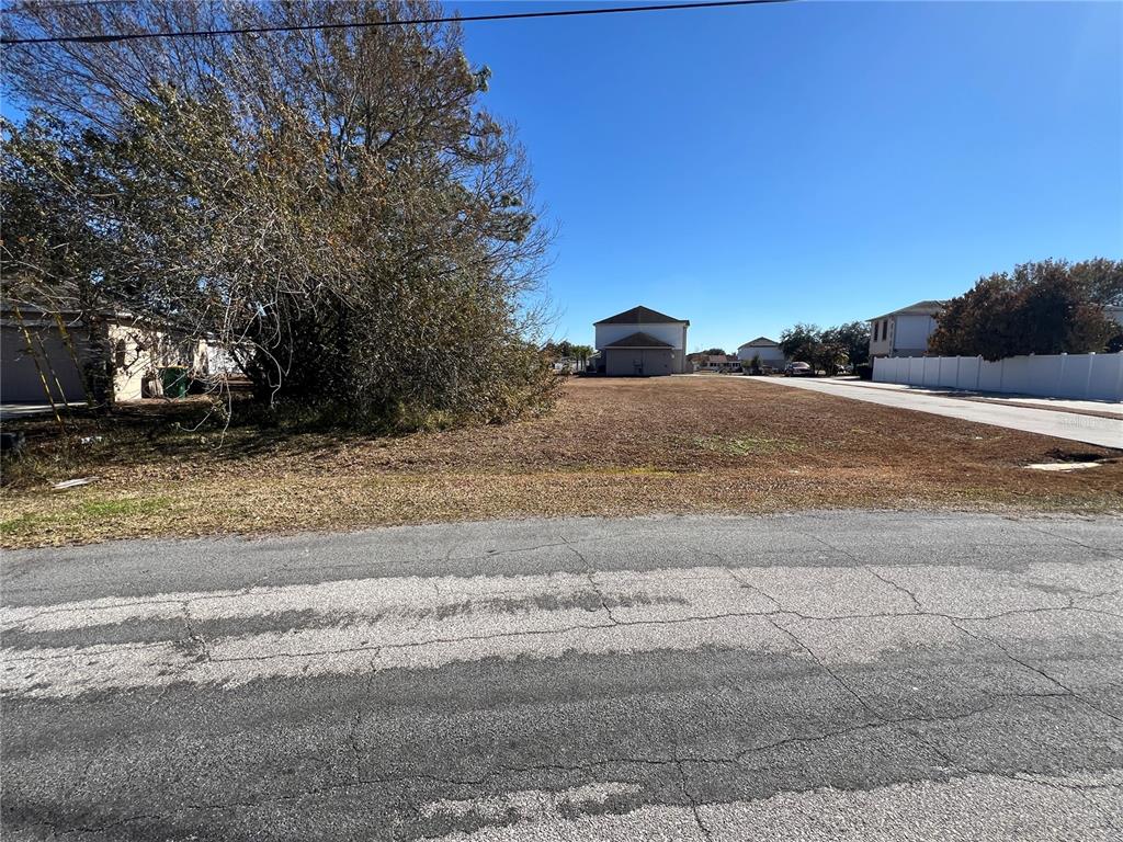 A vacant, grassy residential lot sits between two houses along a paved street — DERBYSHIRE DRIVE, KISSIMMEE, FL