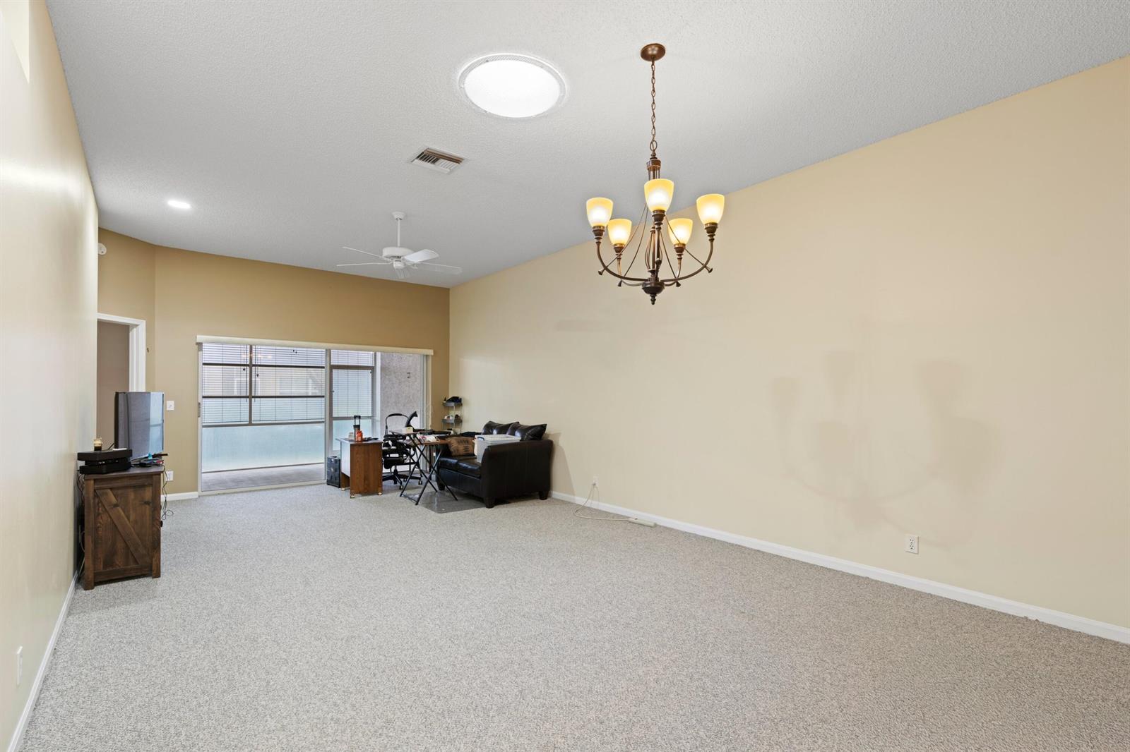 A spacious living room features beige walls, carpeted flooring, a chandelier, and a sliding glass door — 6419 Long Key Lane, Boynton Beach FL 33472, BOYNTON BEACH, FL