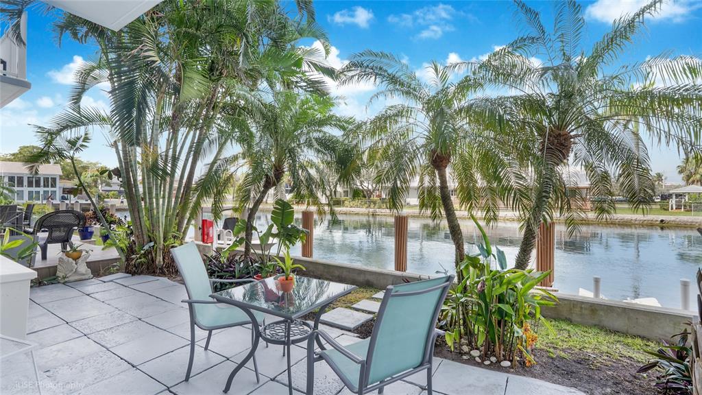A patio with a glass table and chairs overlooks a canal lined with palm trees — 535 HENDRICKS ISLE UNIT 108, FORT LAUDERDALE, FL
