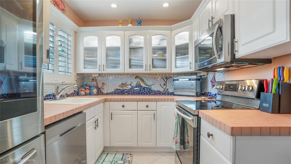A kitchen features white cabinets, tiled countertops, a mosaic backsplash, and stainless steel appliances — 535 HENDRICKS ISLE UNIT 108, FORT LAUDERDALE, FL