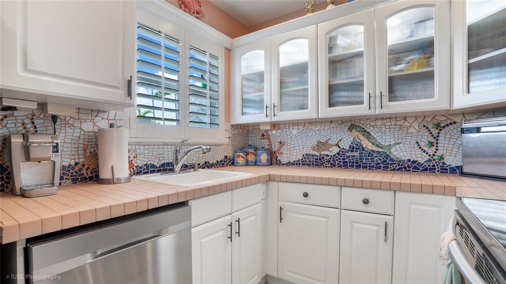 A kitchen features white cabinets, tiled countertops, and a decorative mosaic backsplash with sea life — 535 HENDRICKS ISLE UNIT 108, FORT LAUDERDALE, FL