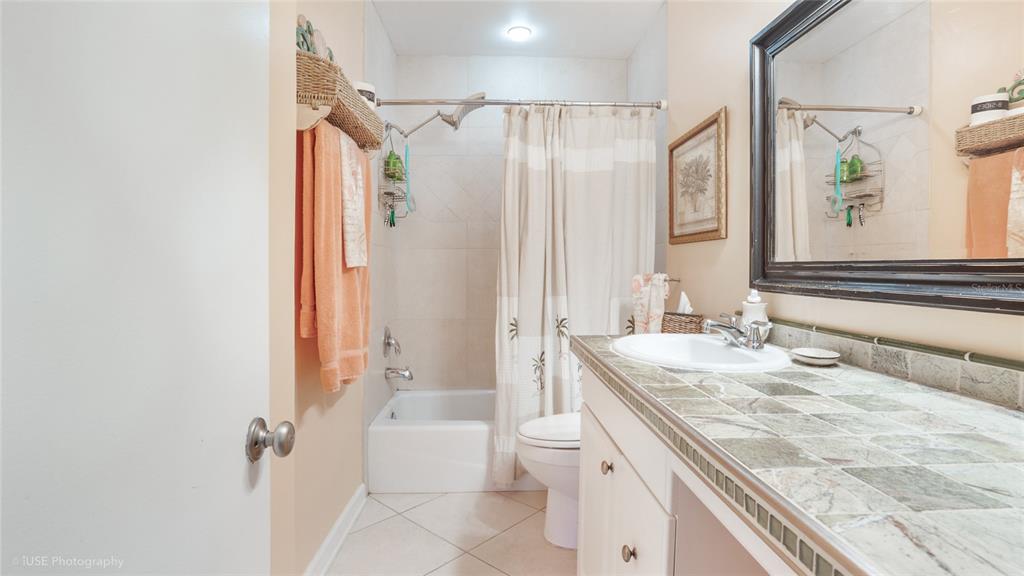 A bathroom features a tiled vanity, a shower-tub combination with a curtain, and light-colored walls — 535 HENDRICKS ISLE UNIT 108, FORT LAUDERDALE, FL