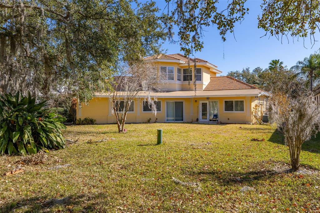 The exterior rear view of a two-story yellow house with a tiled roof and lawn — 2747 KISSIMMEE BAY CIRCLE, KISSIMMEE, FL
