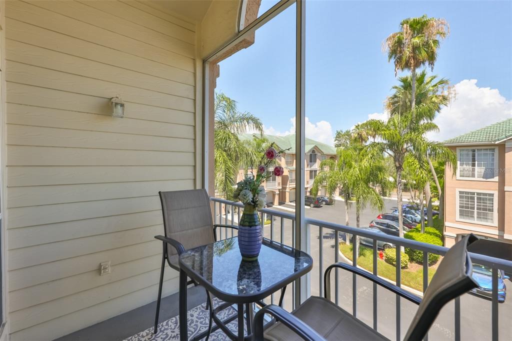 A screened-in balcony features a small glass table, two chairs, and views of palm trees — 3312 BAY CLUB CIRCLE UNIT 3312, TAMPA, FL