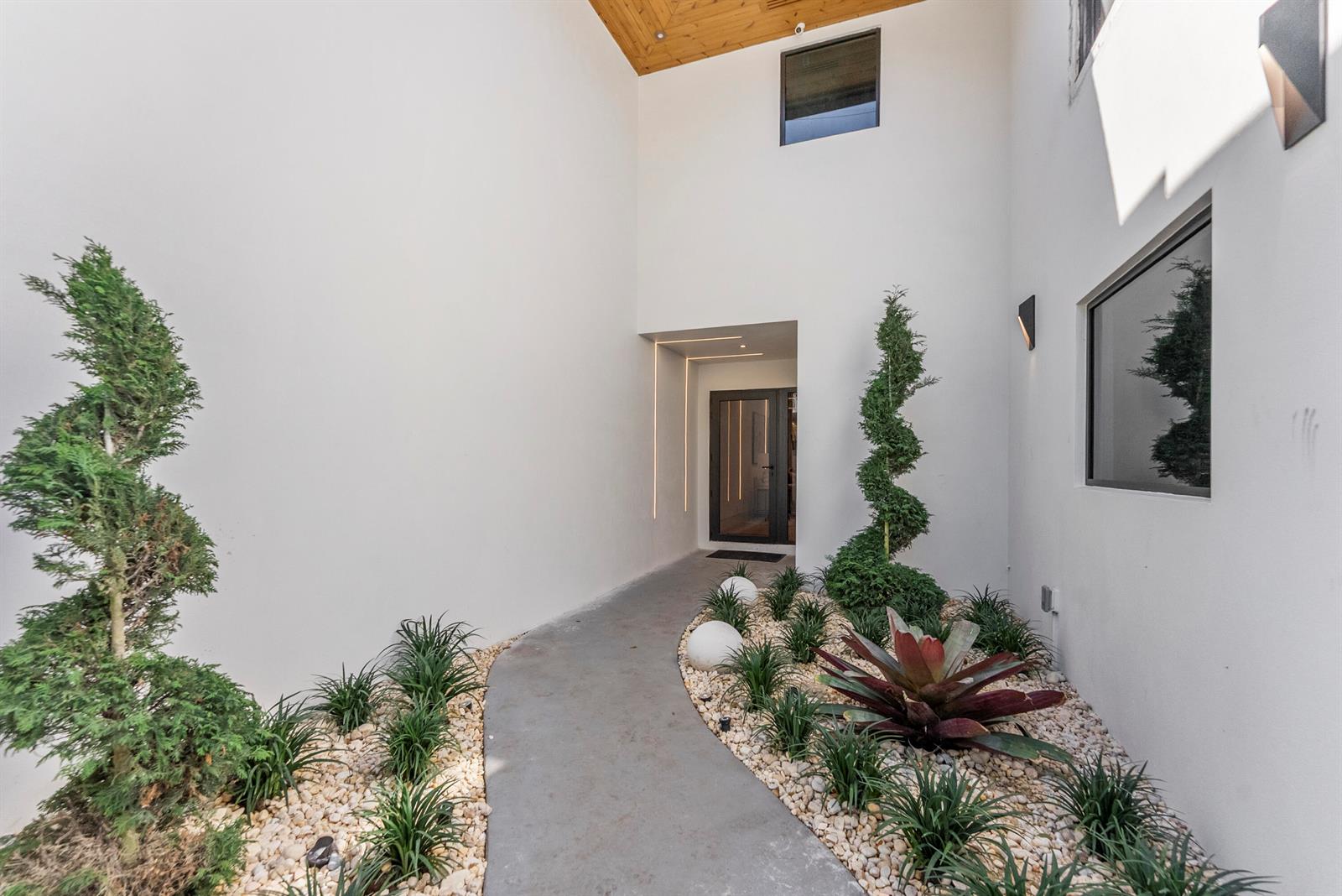 A concrete walkway leads to a modern entryway flanked by spiral topiaries and white walls — 1690 S Ocean Boulevard, Delray Beach FL 33483, DELRAY BEACH, FL