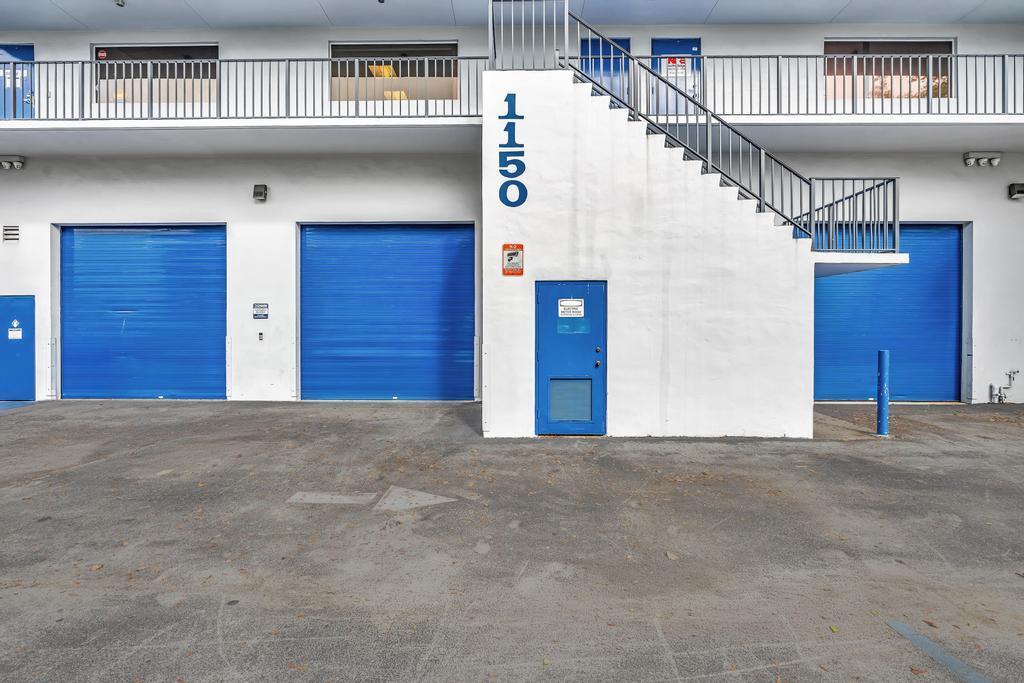 The exterior of a commercial building features blue roll-up doors, a central staircase, and address number 1150 — 1150 SW 10th Avenue, Pompano Beach FL 33069, POMPANO BEACH, FL