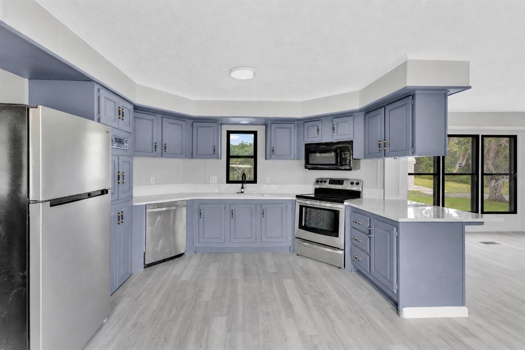 A kitchen features blue cabinets, stainless steel appliances, white countertops, and light wood-look flooring — 9185 CONCORD ROAD, ST CLOUD, FL