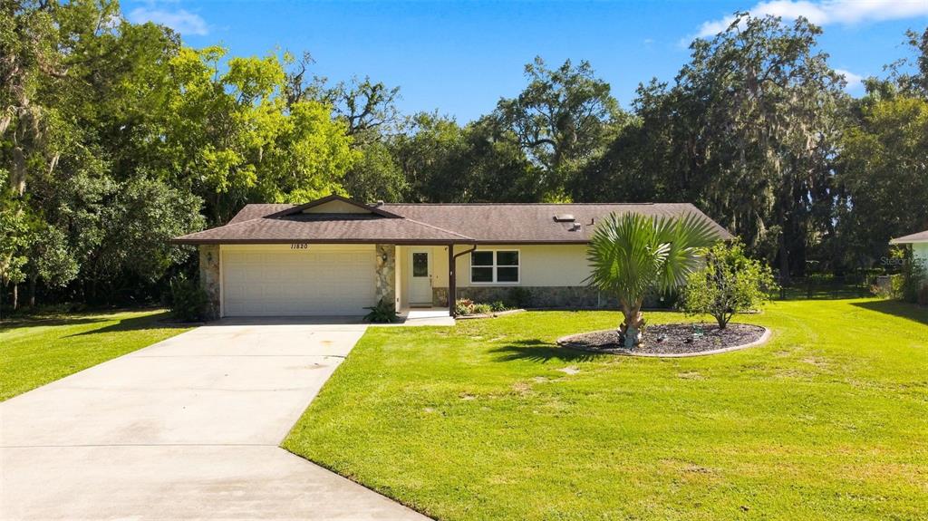 A single-story house with a two-car garage, stone accents, and a large front lawn — 11820 W FISHERMAN LANE, HOMOSASSA, FL