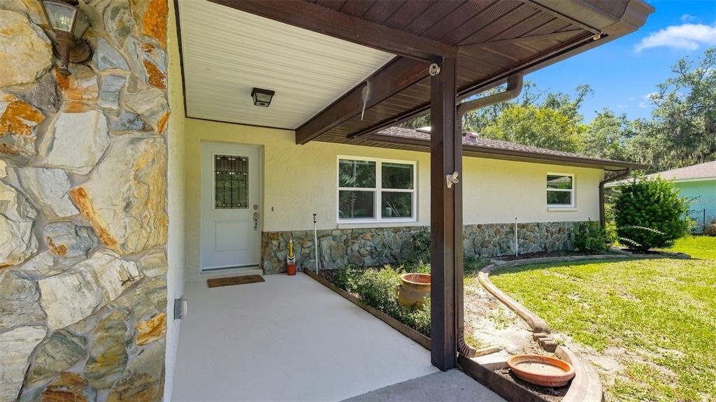 A covered concrete porch leads to a white front door on a stone-accented house exterior — 11820 W FISHERMAN LANE, HOMOSASSA, FL