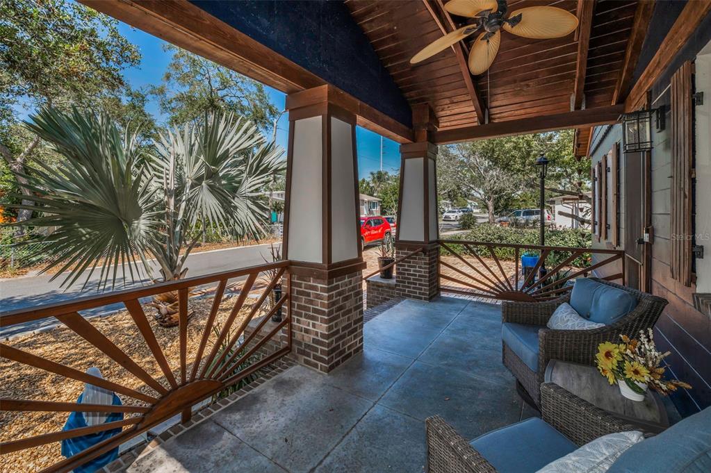 A covered porch features a wooden ceiling, brick-based columns, sunburst railings, and wicker patio furniture — 525 LEXINGTON STREET, DUNEDIN, FL