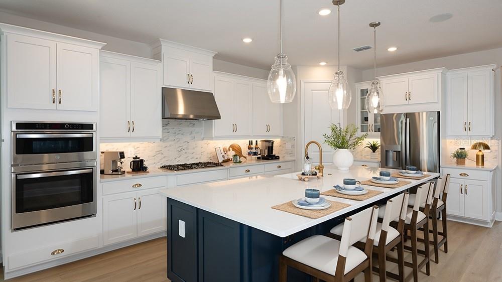 A modern kitchen features white cabinetry, a dark blue island, stainless steel appliances, and pendant lighting — 12711 DOCKYARD TRAIL, PALMETTO, FL