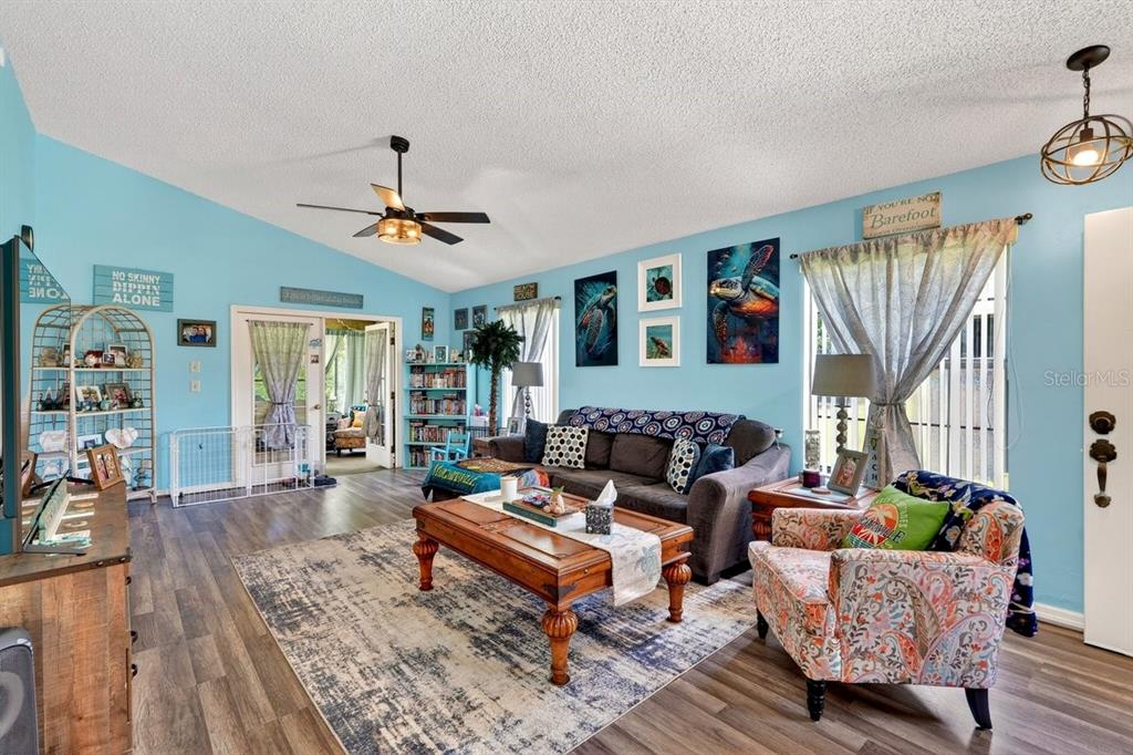 A living room with light blue walls, wood-look flooring, a ceiling fan, and coastal decor — 188 GRAY DOVE COURT, DAYTONA BEACH, FL