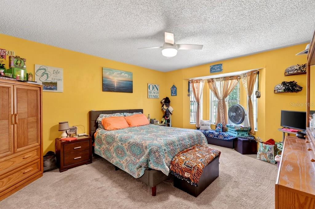 A bedroom with yellow walls, a queen bed, a ceiling fan, and a bay window — 188 GRAY DOVE COURT, DAYTONA BEACH, FL