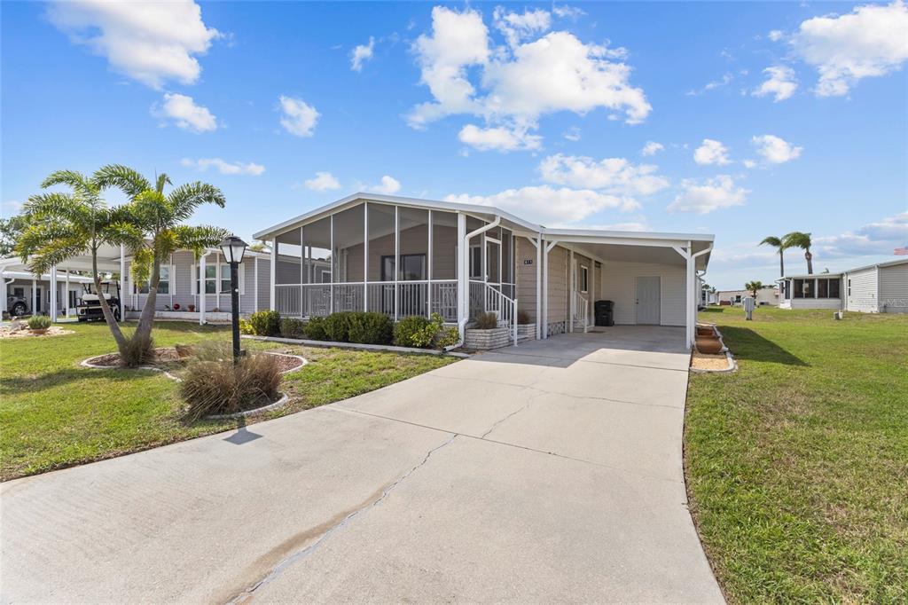 A single-story manufactured home features a screened-in front porch, a concrete driveway, and a carport — 611 LA JOLLA CIRCLE, NORTH PORT, FL