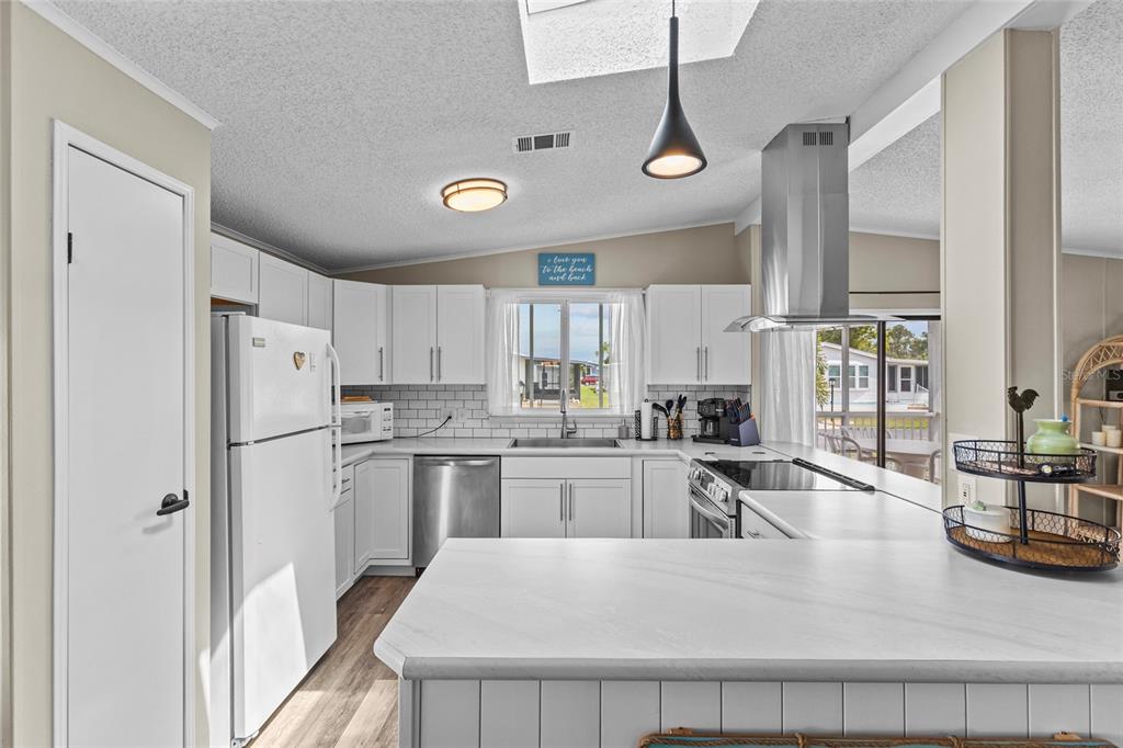 A kitchen with white cabinets, stainless steel appliances, a subway tile backsplash, and a peninsula — 611 LA JOLLA CIRCLE, NORTH PORT, FL