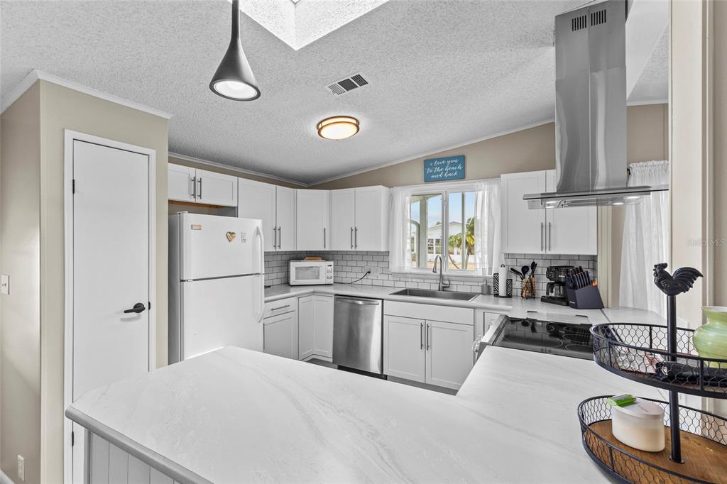 A bright kitchen features white cabinets, stainless steel appliances, a subway tile backsplash, and countertops — 611 LA JOLLA CIRCLE, NORTH PORT, FL