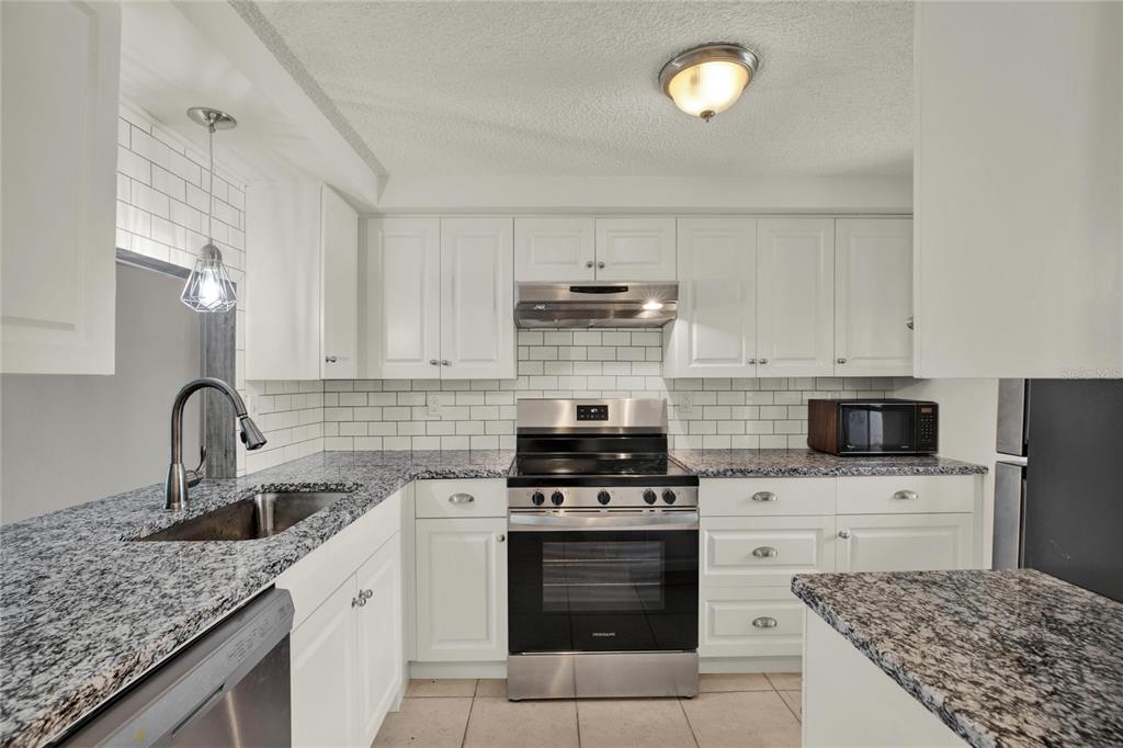 A kitchen with white cabinets, granite countertops, stainless steel appliances, and a subway tile backsplash — 4115 HAMPTON DRIVE UNIT n/a, NEW PORT RICHEY, FL